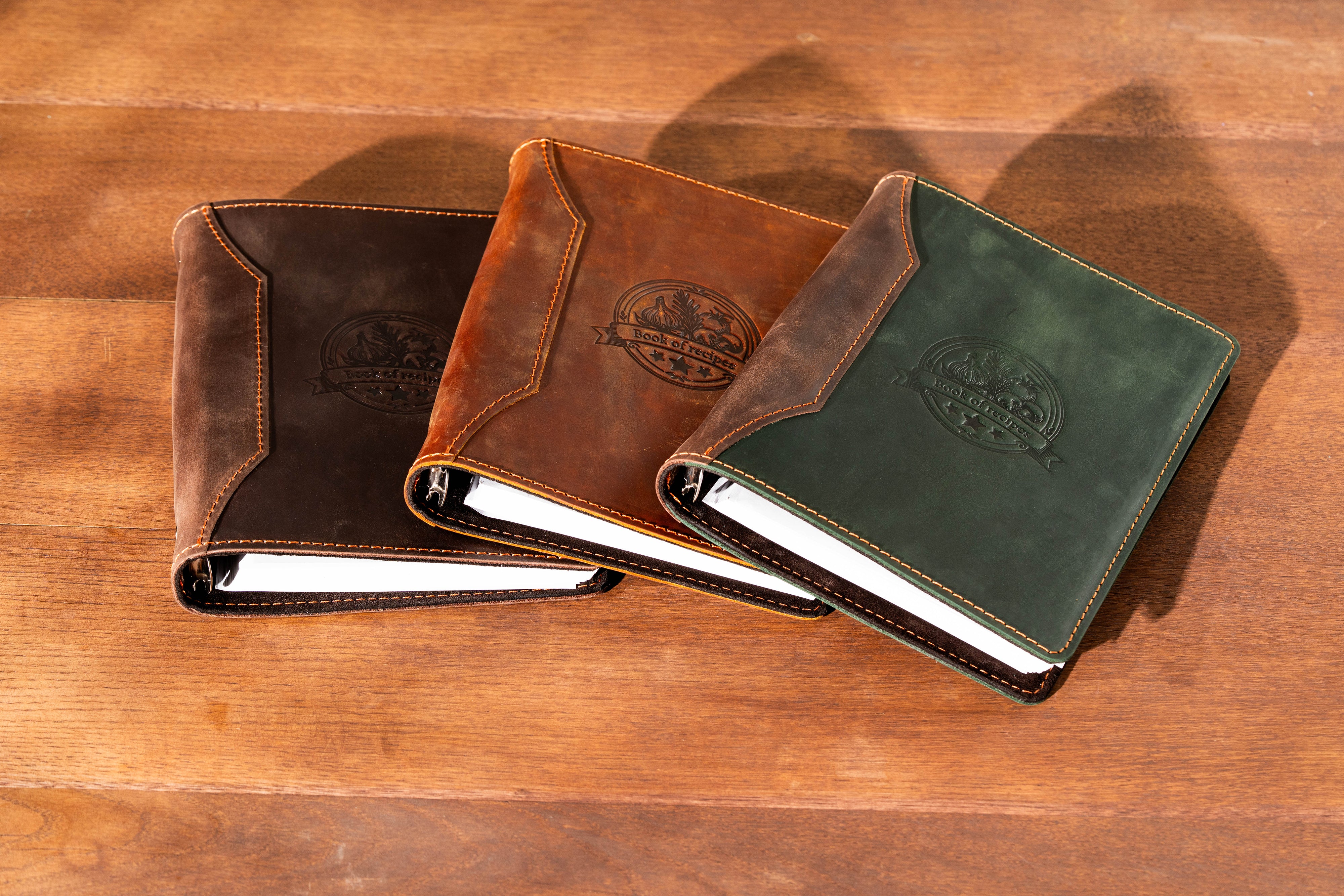 Three leather-bound notebooks in brown, tan, and green