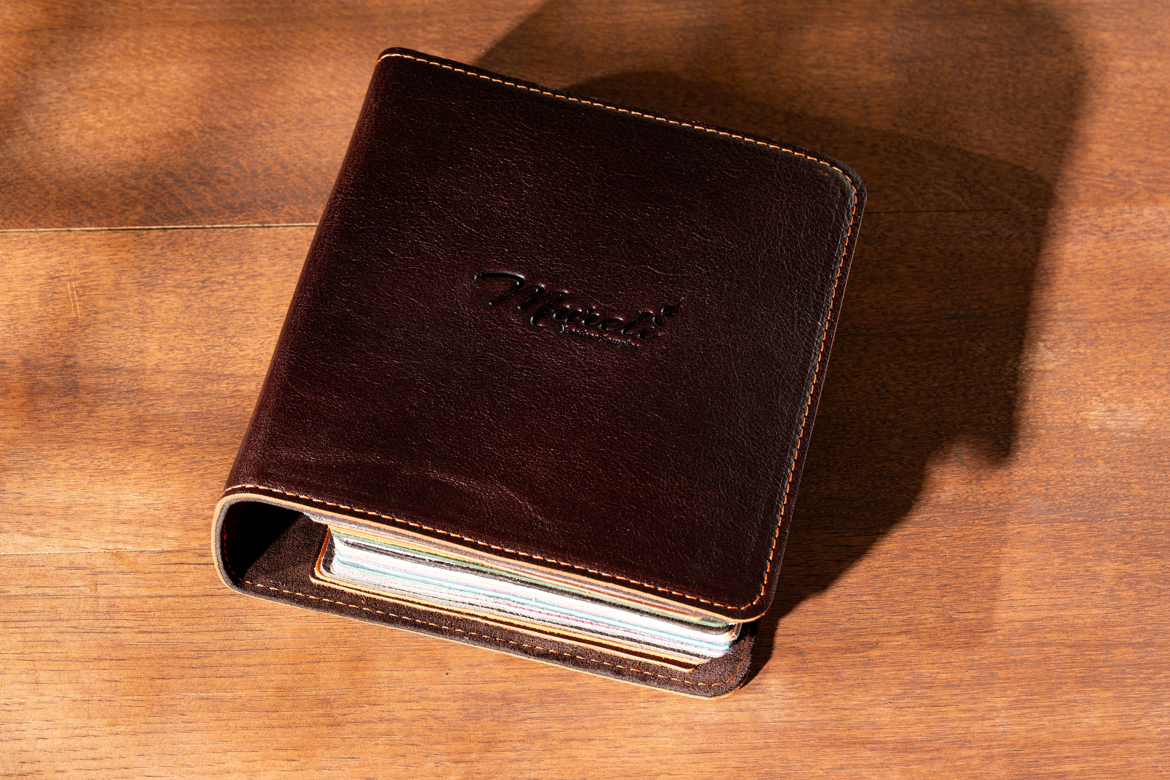 Dark brown Mureli leather sample binder with stitched cover and colorful leather swatches inside