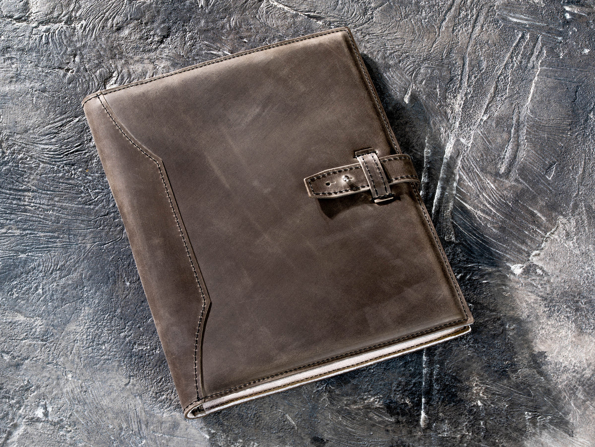 Gray personalized leather portfolio and padfolio with strap closure on textured dark surface