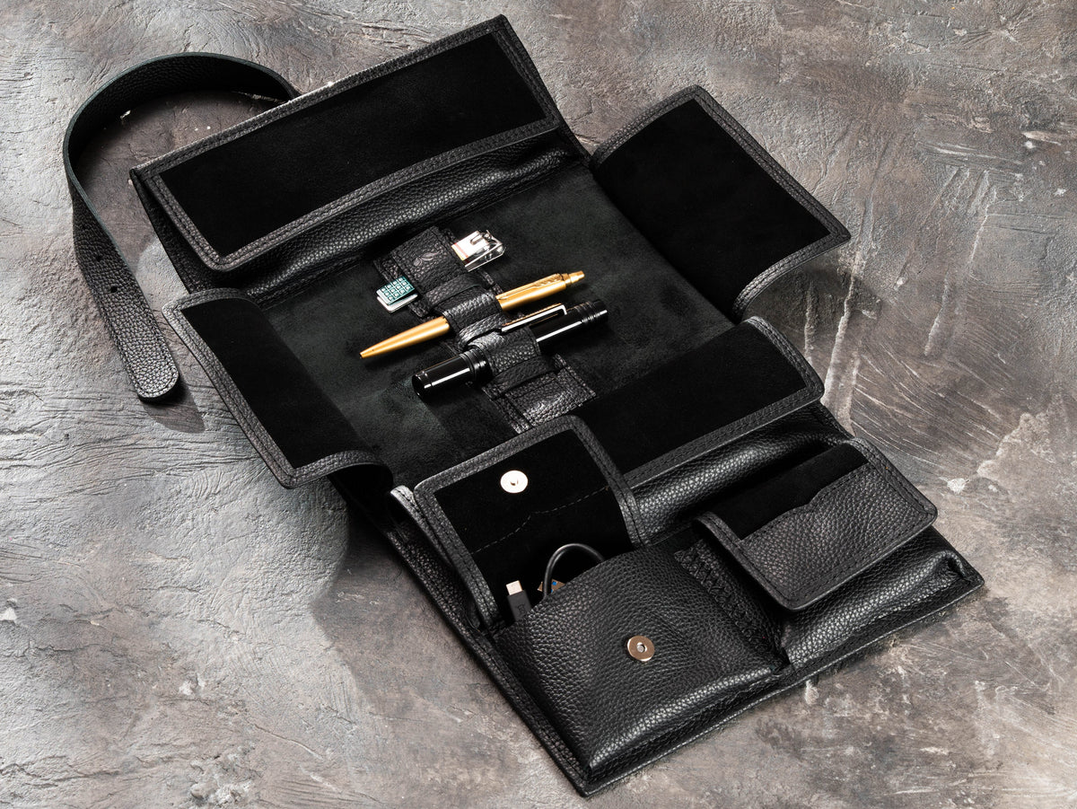 Black hanging roll-up leather travel organizer with open pockets, elastic holders and men's travel accessories