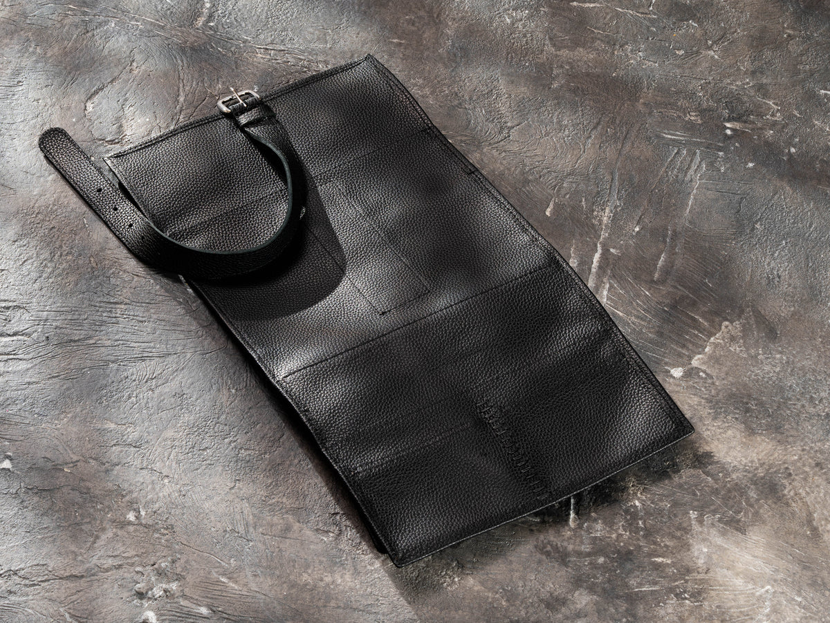 Black leather travel organizer opened flat showing exterior, buckle strap and reinforced hand stitching