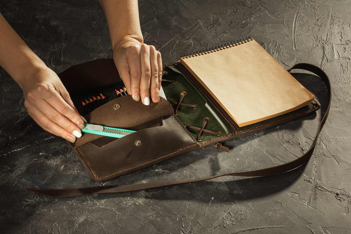 Open green and brown leather artist organizer with 12 colored pencils and horizontal A5 sketchbook
