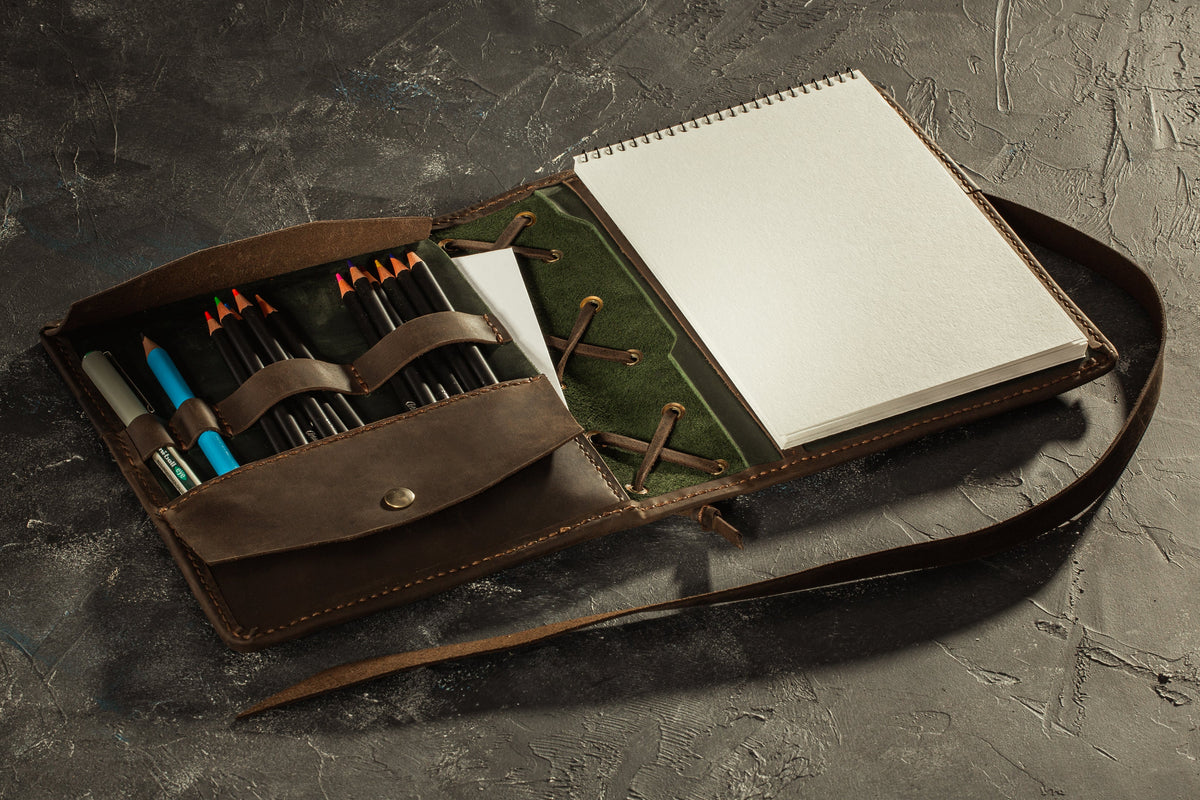 Closed green and brown leather sketchbook organizer with wrap strap and sample personalized name tag