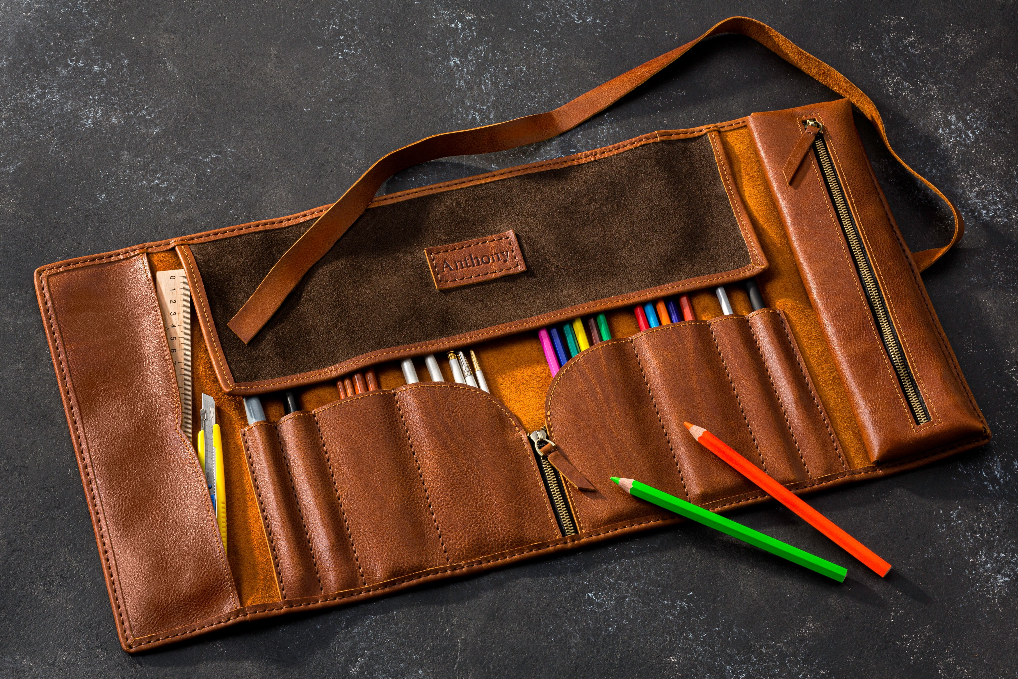 Brown leather pencil case with colorful pencils on a dark surface
