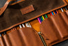 Brown leather pencil case with  branding, containing colored pencils.
