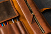 Brown leather pencil case with colorful pencils and a zipper on a dark surface