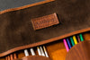 Brown leather pencil case with 'Anthony' branding and colorful pencils inside.