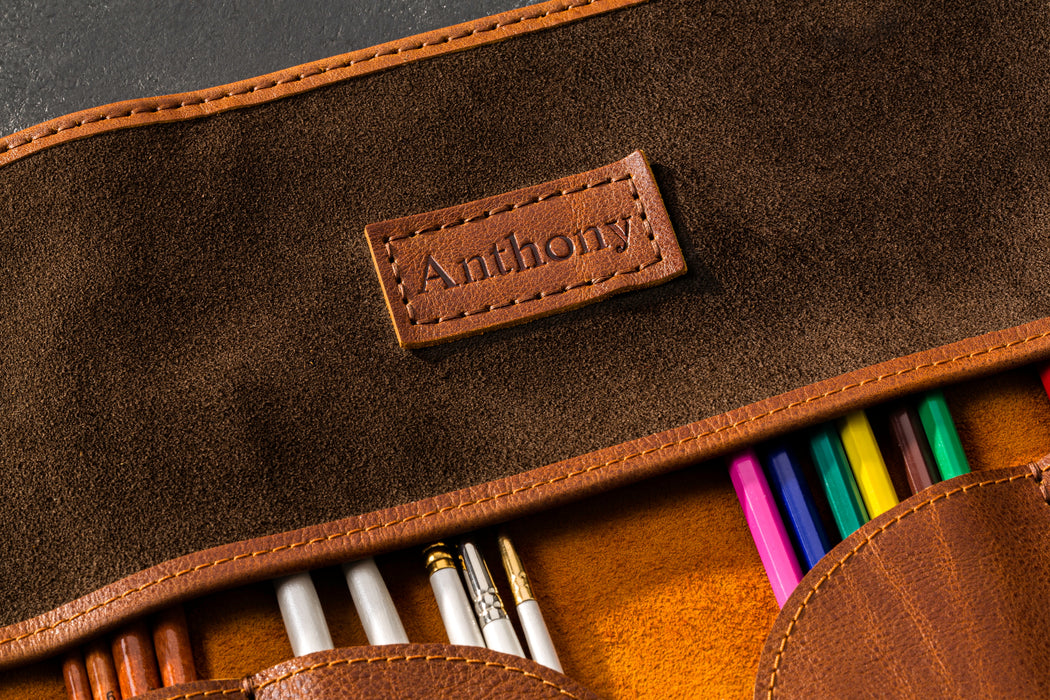 Brown leather pencil case with 'Anthony' branding and colorful pencils inside.