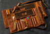 Two personalized leather artist roll organizers in Cognac Brown with brushes, pencils, and tools inside — handcrafted and labeled