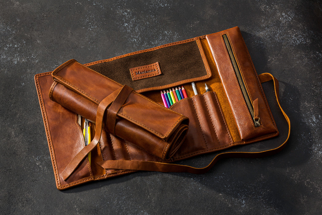 Two Brown leather pencil roll with colorful pencils on a dark surface