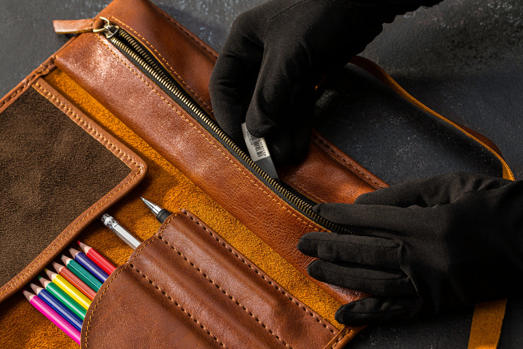 Brown leather case with colorful pencils and a hand wearing a black glove opening it.