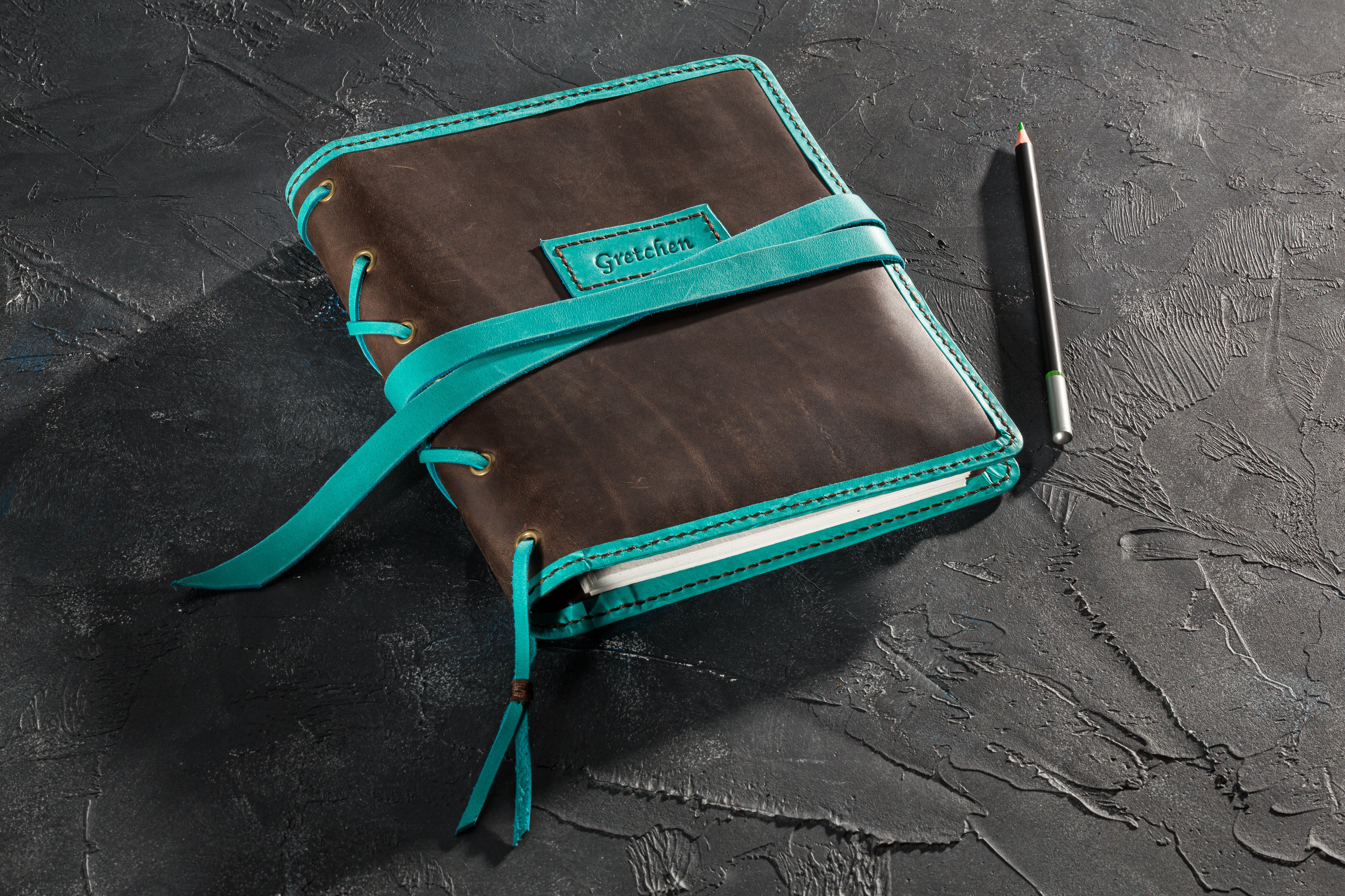 Closed leather journal wrapped with long turquoise strap, personalized name patch visible