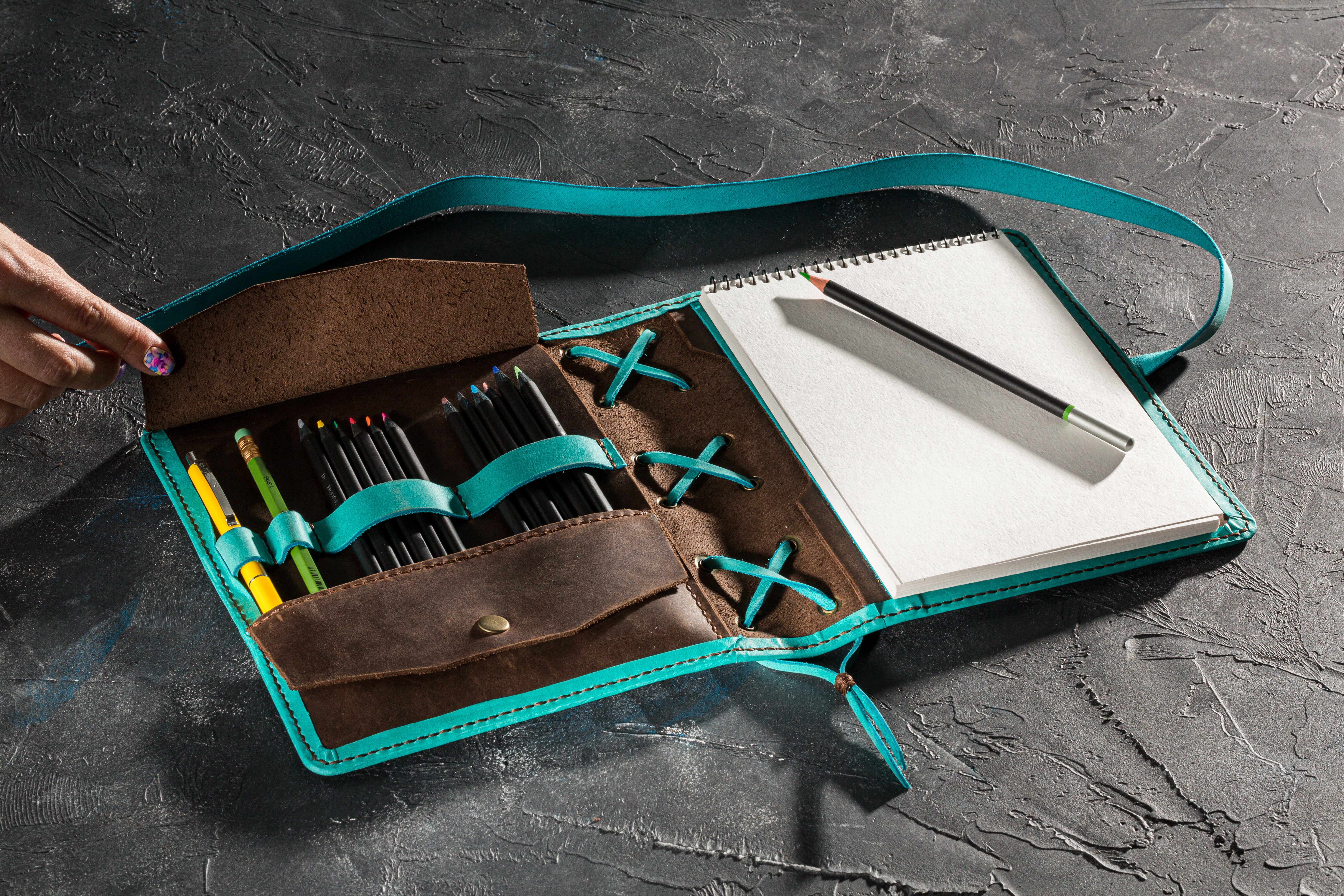 Leather organizer opened with hand lifting pocket flap, pencil slots and A5 spiral sketchpad
