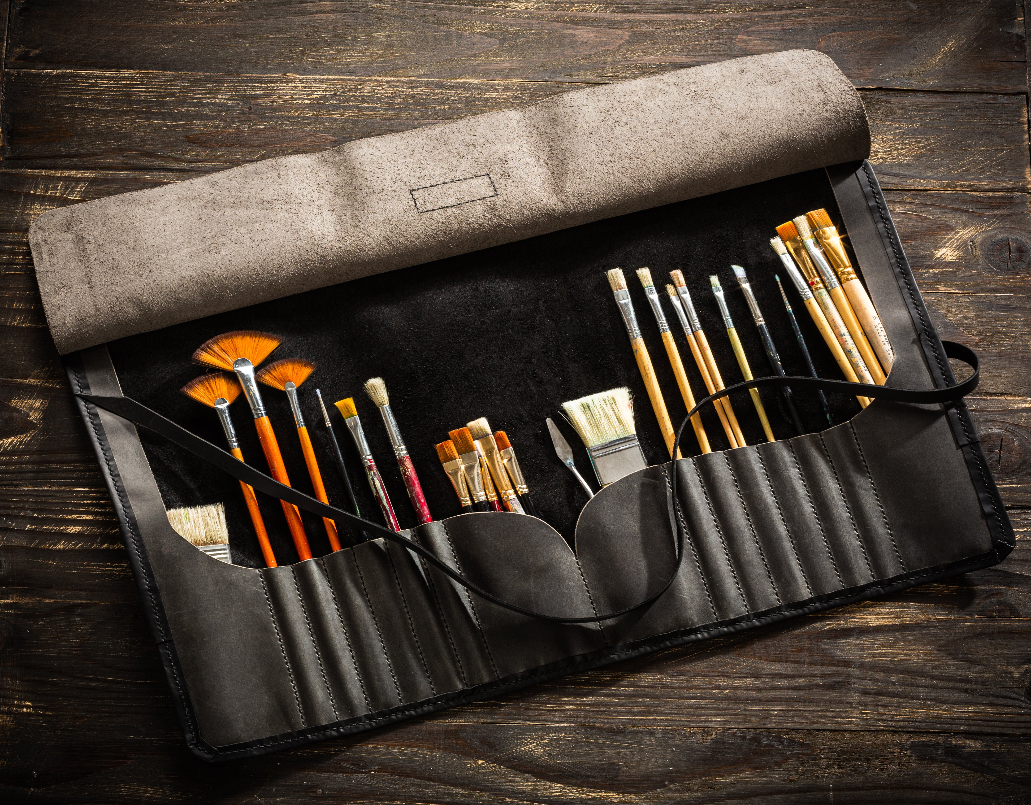 Open black leather artist roll with suede interior and brushes organized