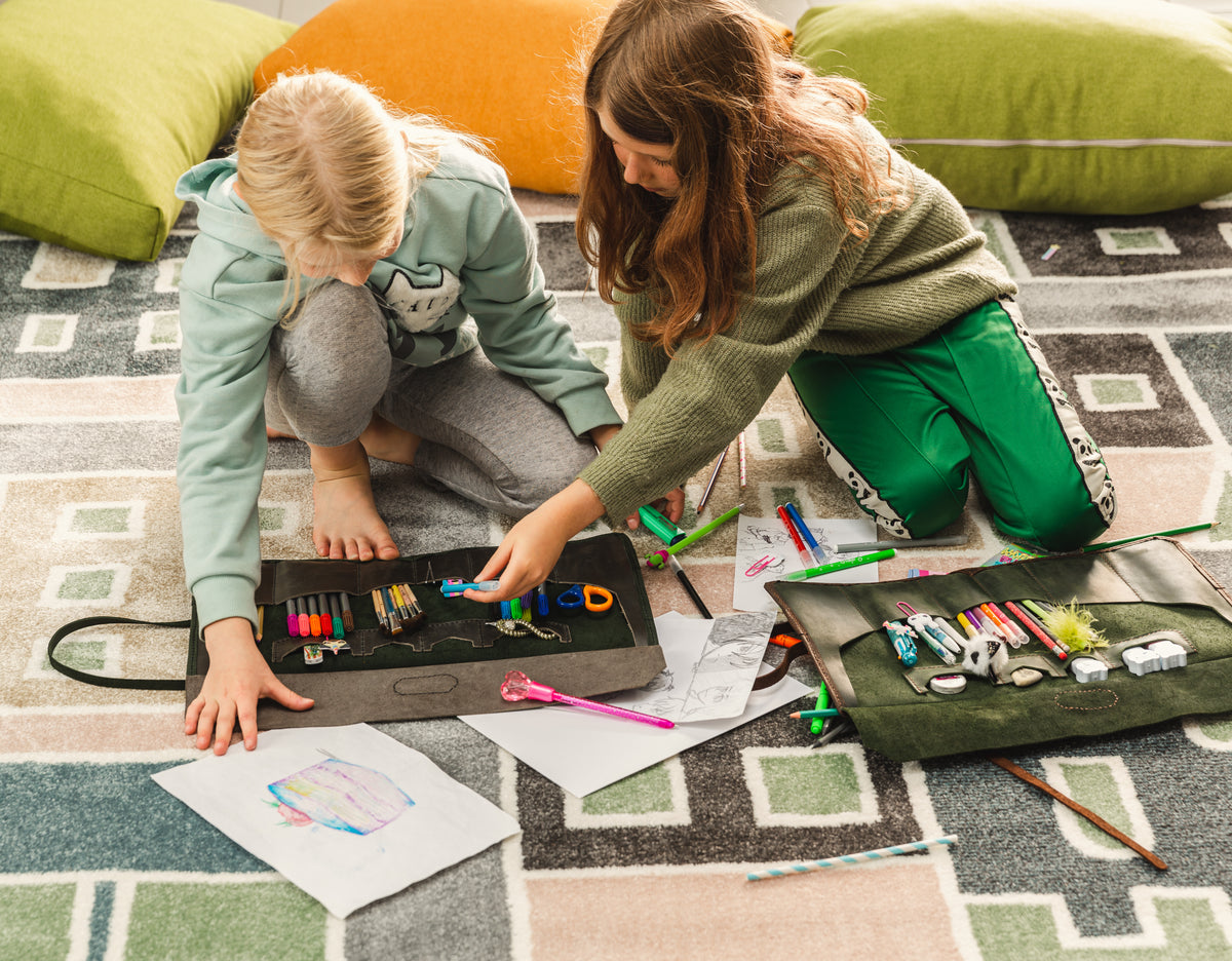 Two young artists using olive green and black leather artist tool rolls with pencils, markers and drawing supplies