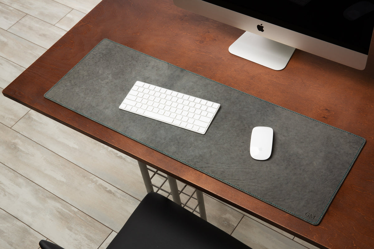 Gray leather desk mat with celeste blue stitching and custom monogram on a wooden desk with keyboard and mouse