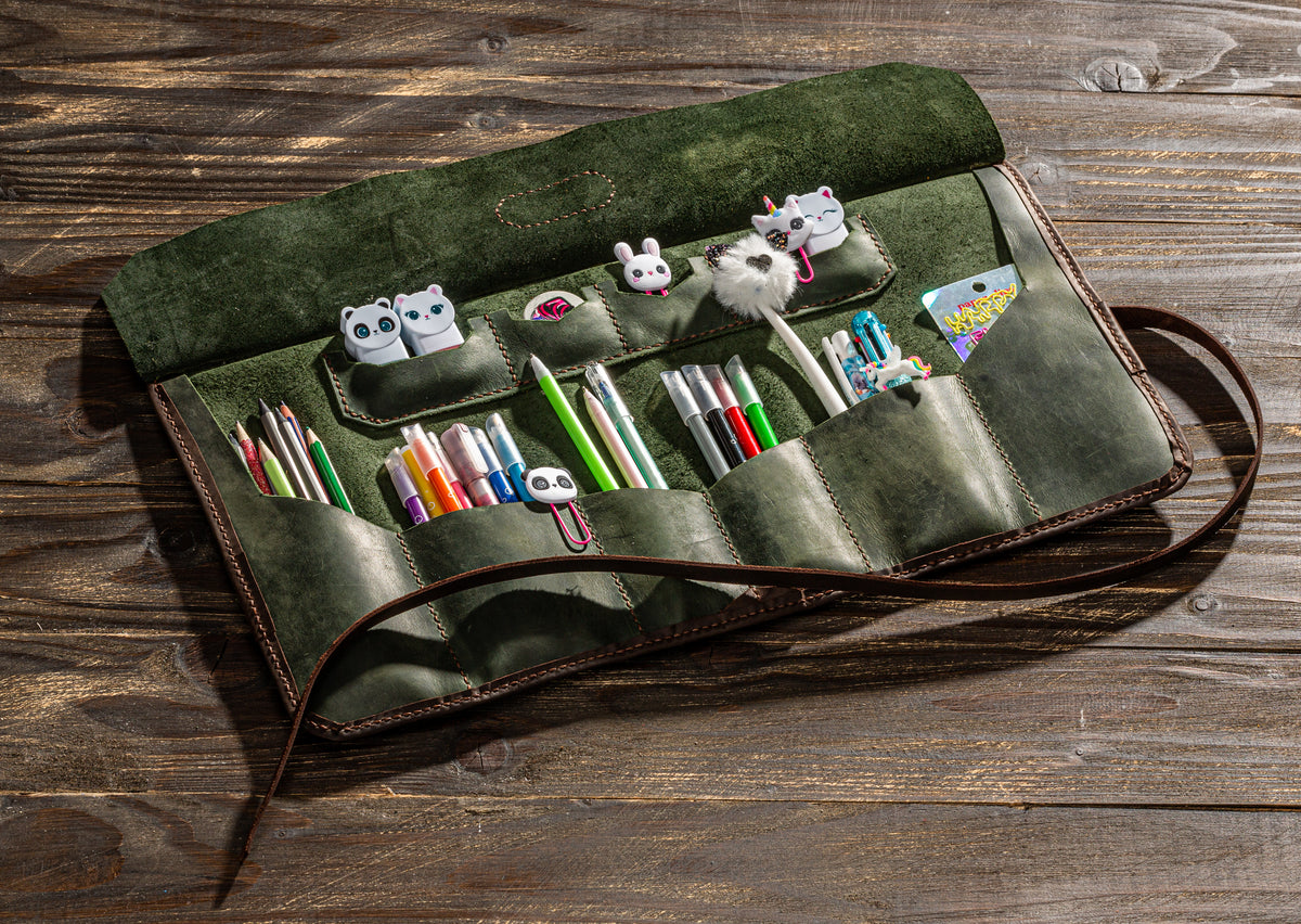 Open olive green leather artist roll with brown edging, multiple tool pockets and long wrap strap