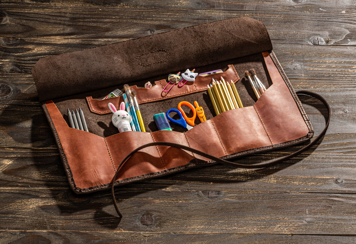 Open copper and brown leather artist tool organizer with multiple pockets for pencils, brushes and art tools