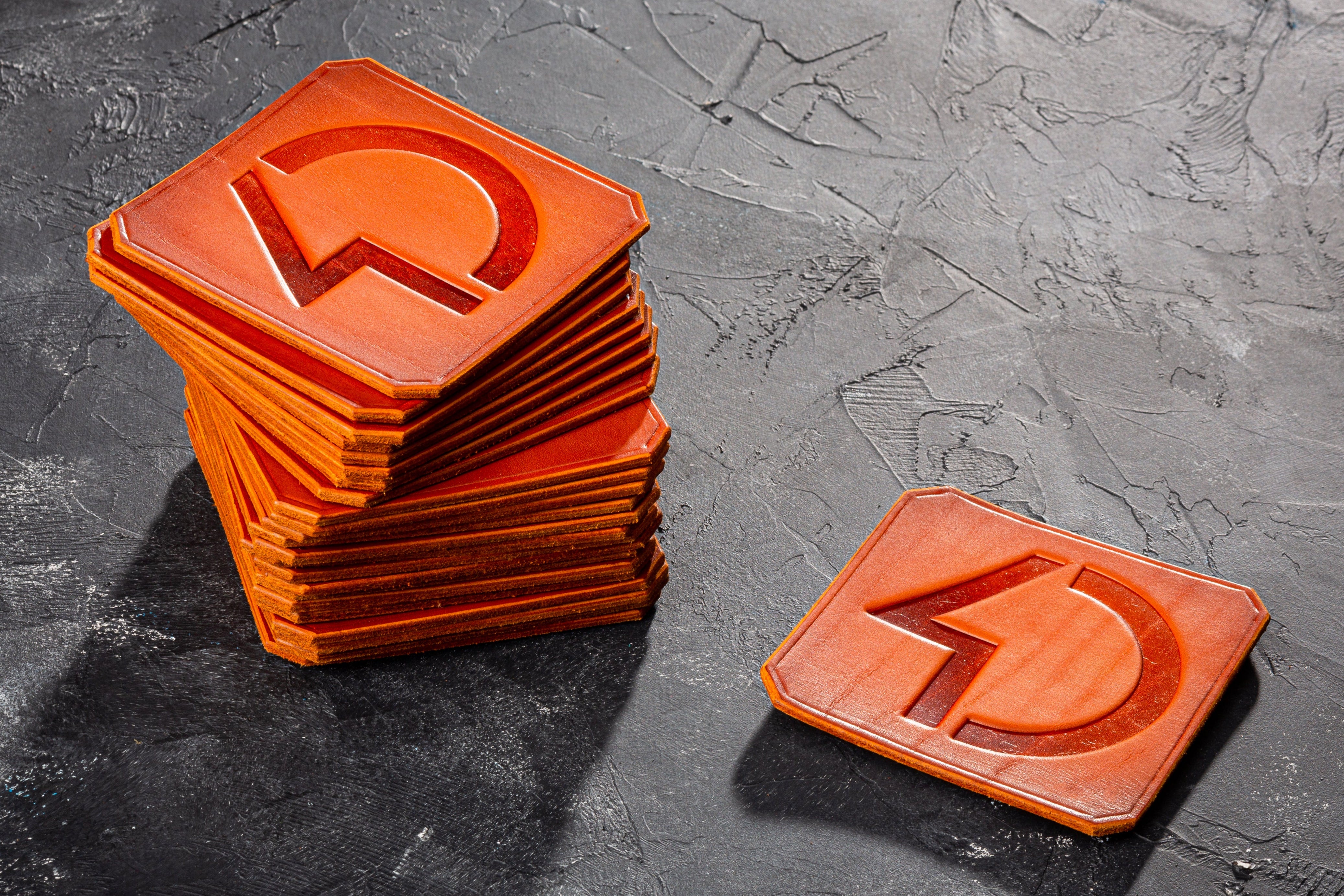 Stack of orange square coasters with a central cutout on a dark textured surface