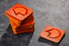 Stack of orange square coasters with a central cutout on a dark textured surface