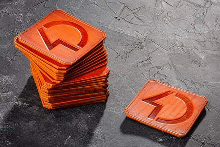 Stack of orange square coasters with a central cutout on a dark textured surface