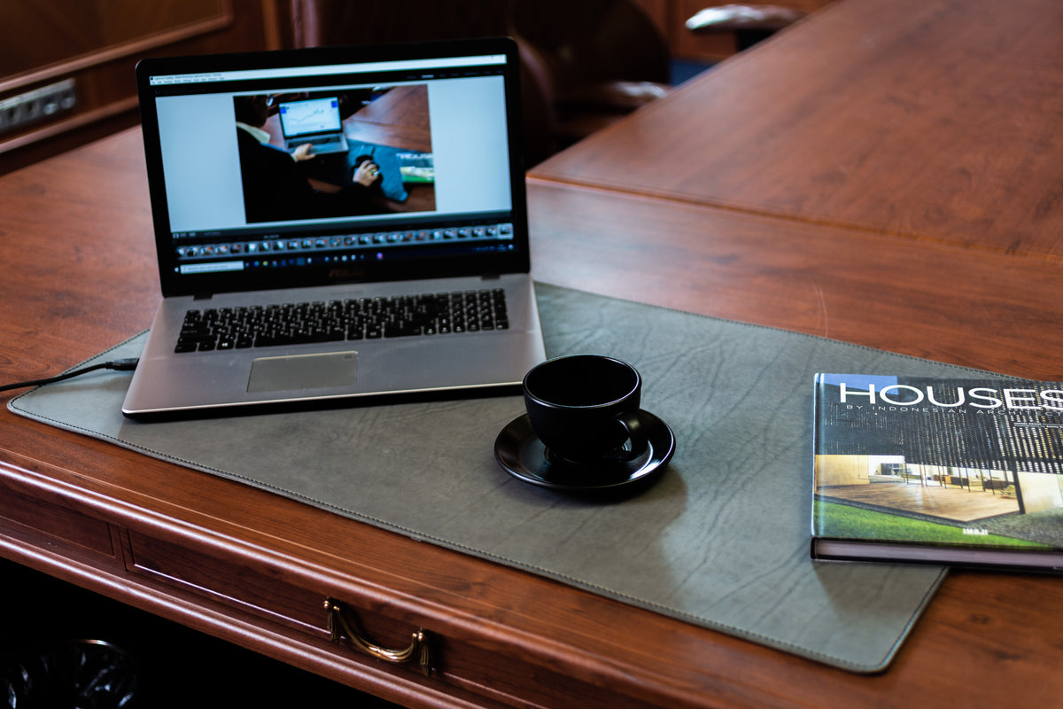 Large gray leather desk mat on executive wooden desk with laptop, coffee cup and book
