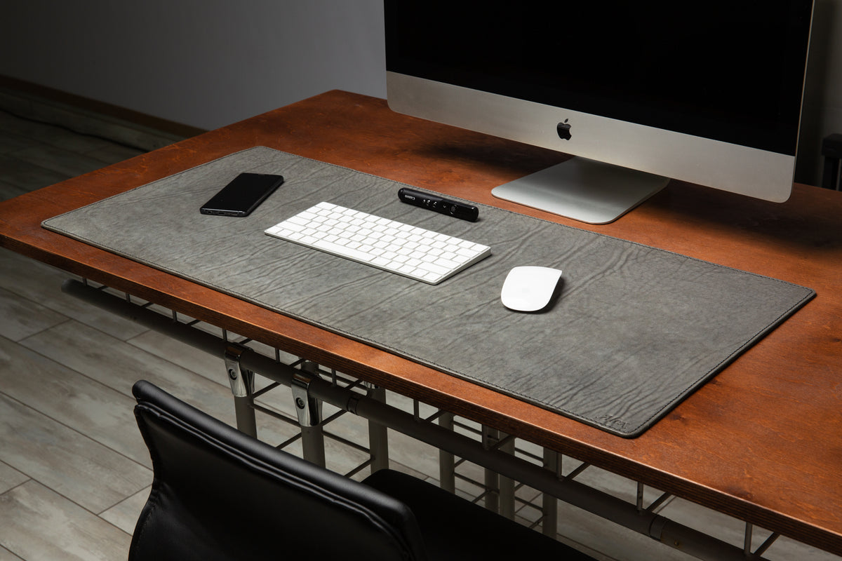 Large gray leather desk mat with celeste blue stitching and custom monogram in a modern workspace