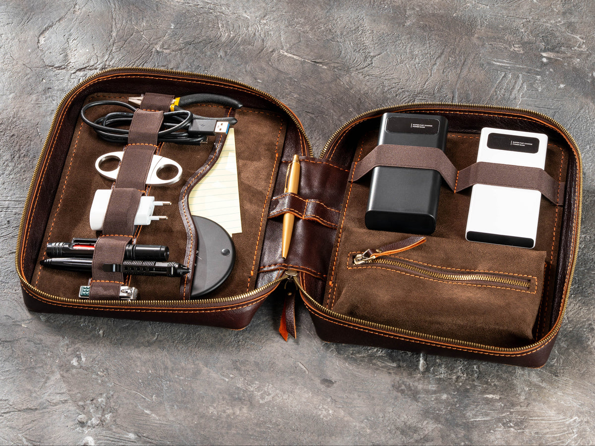 Open Dark Cognac leather travel organizer filled with chargers, power banks, cables and men’s travel essentials