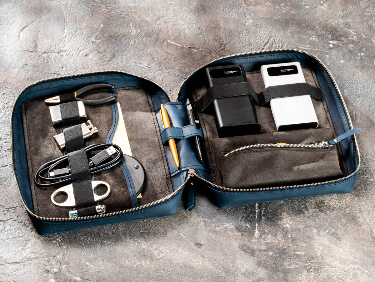 Deep Blue zippered leather travel organizer filled with chargers, cables, tools and everyday travel essentials