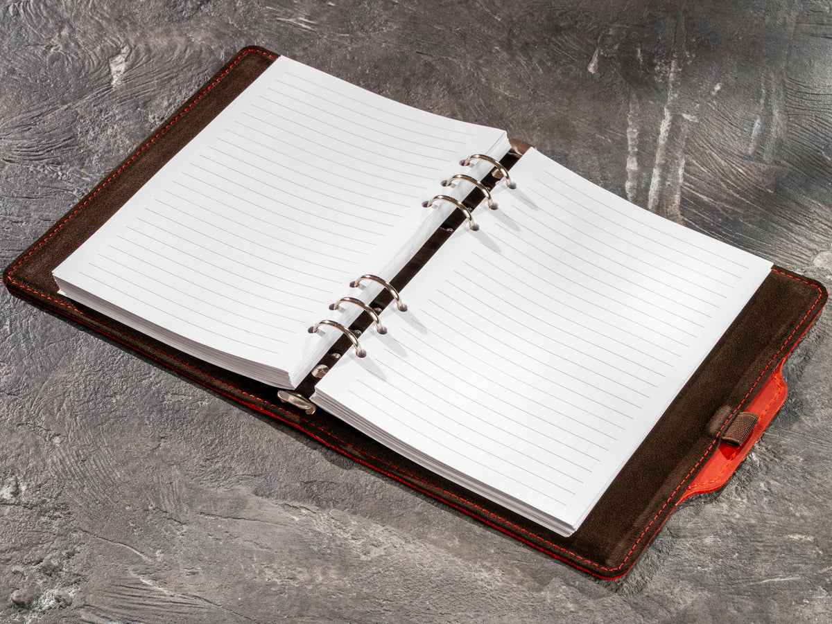 Open red leather business notebook with handwritten lined page and gold pen