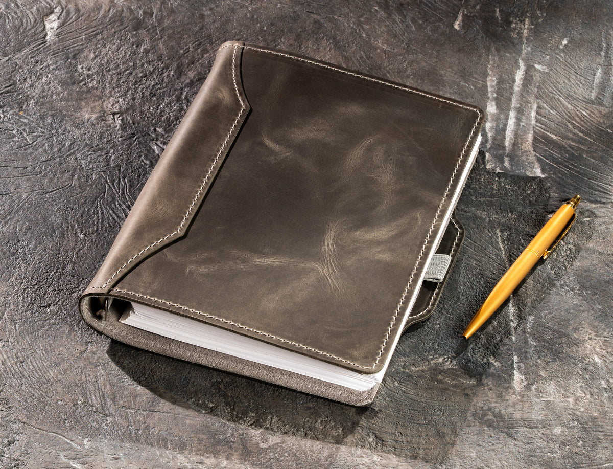 Gray refillable leather business notebook with gold pen beside the cover