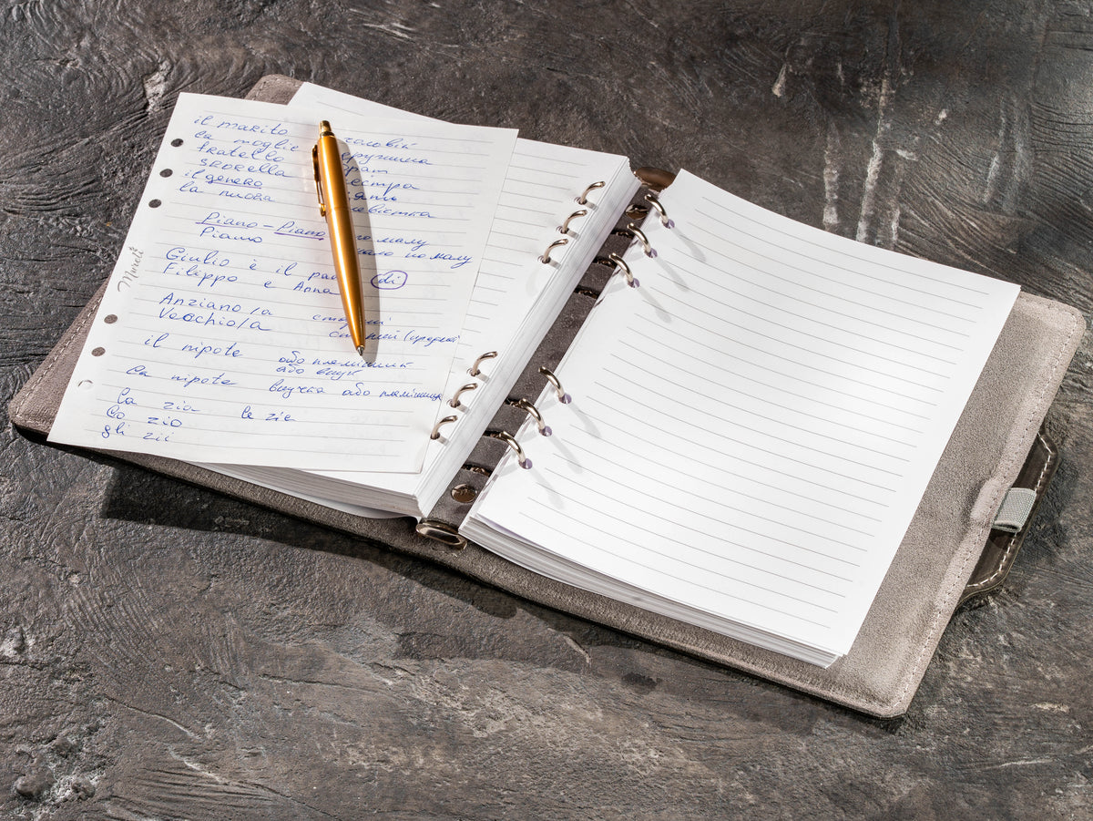 Open gray leather business notebook with handwritten notes and gold pen