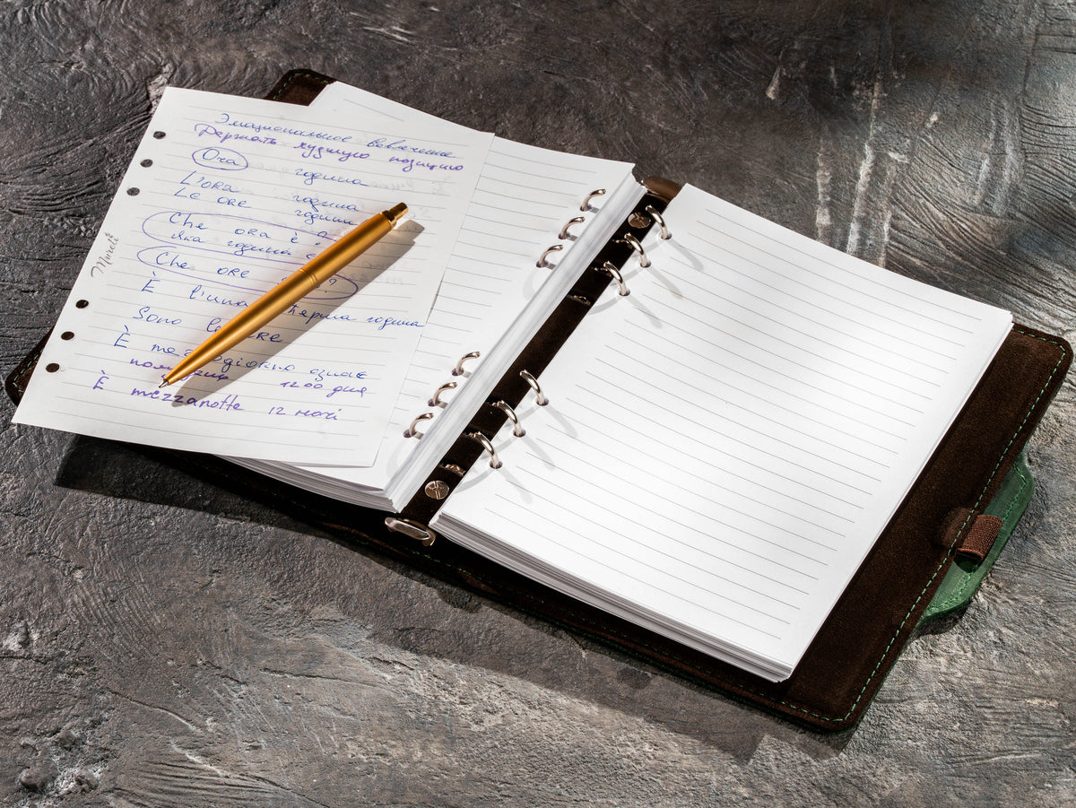 Open green leather notebook with handwritten notes and gold pen