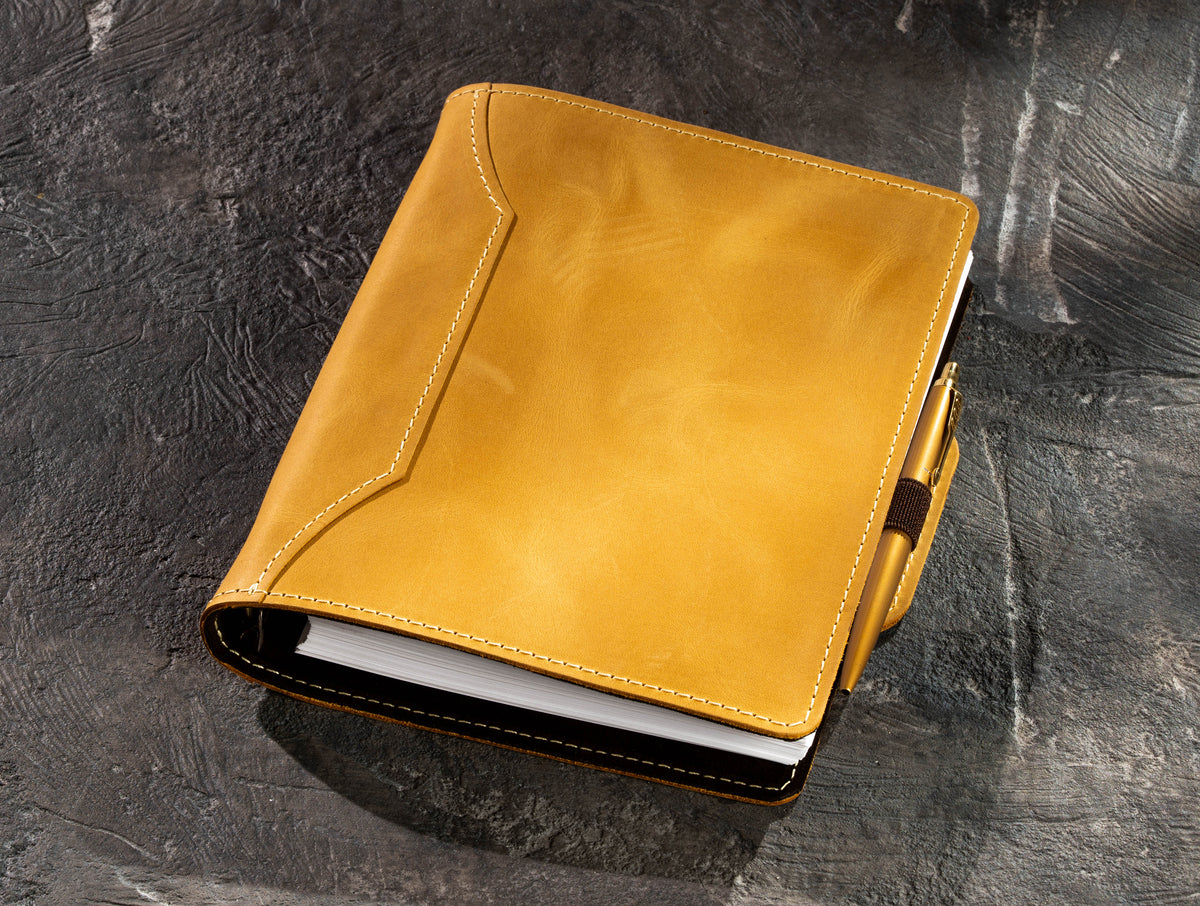 Yellow refillable leather notebook with gold pen secured in integrated elastic pen holder
