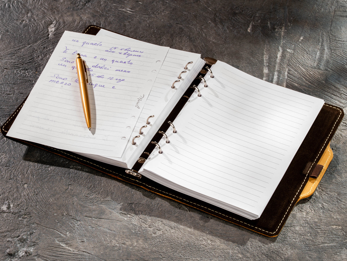 Yellow leather refillable ring binder notebook with handwritten notes, removable pages and gold pen