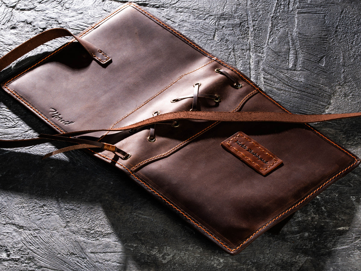Fully opened brown leather artist organizer showing wrap closure, decorative lacing and sample personalized name tag