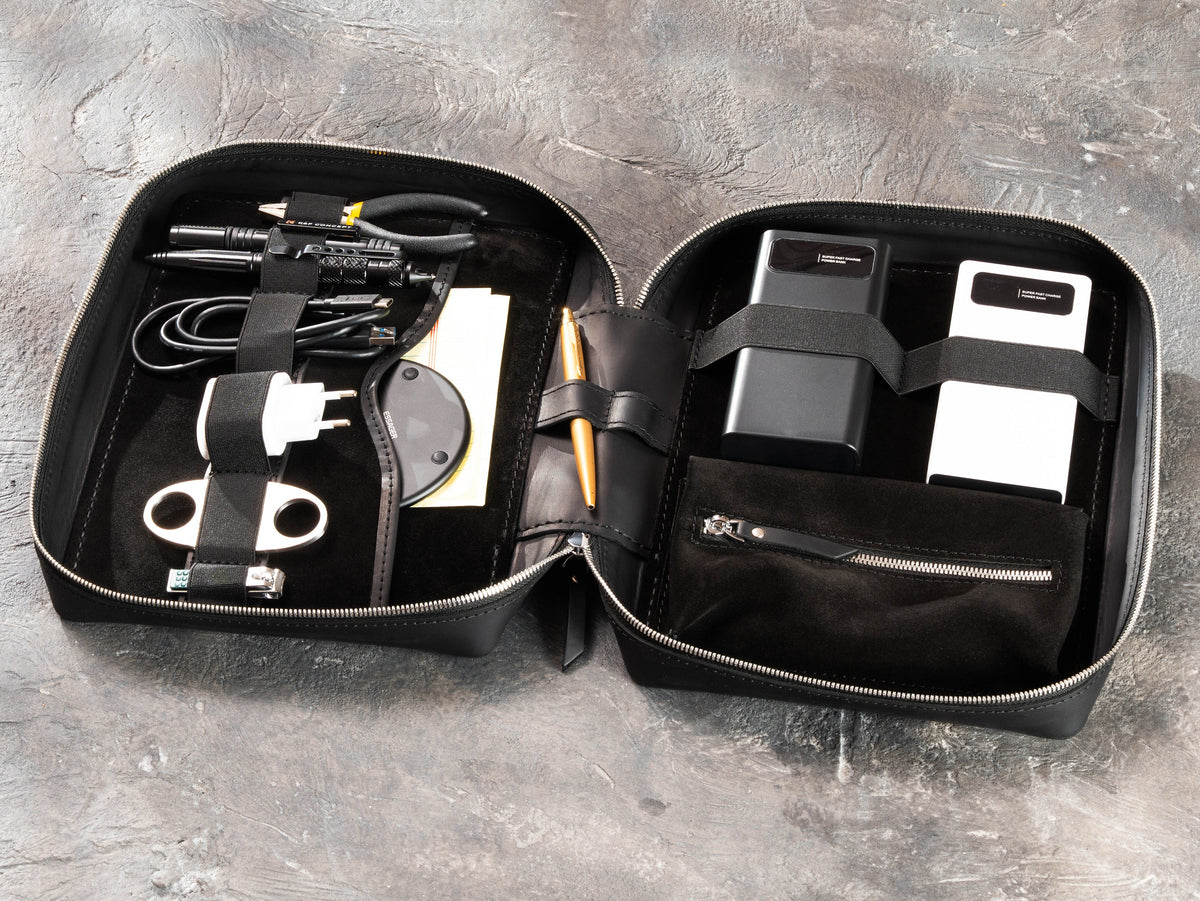Black zippered leather travel organizer filled with chargers, cables, tools and business travel essentials