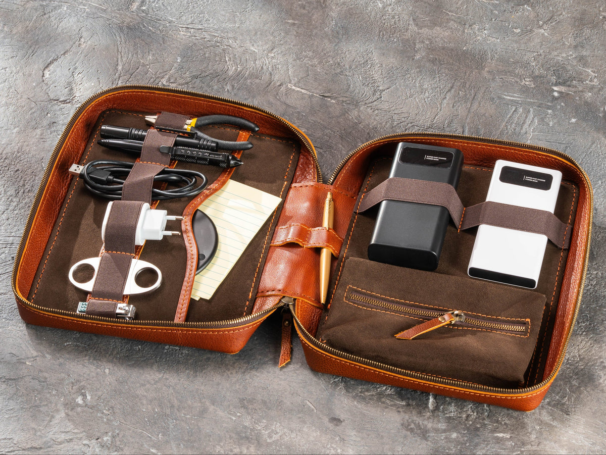 Camel zippered leather travel organizer filled with chargers, cables, grooming accessories and men’s travel essentials